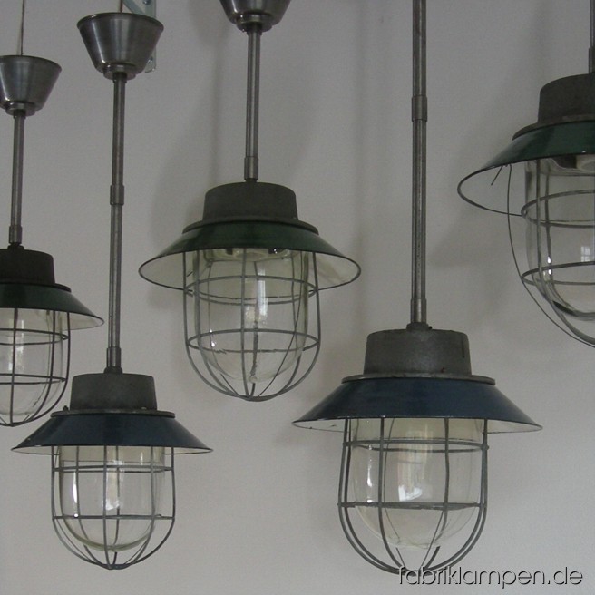 Industrielampen mit blauen oder grünen Emailschirmen und Schutzgittern. Die Lampen sind neu elektrifiziert und haben eine Aufhängung aus Stahlrohr mit Baldachin. Material: Gusseisen, Glas, Stahl, blau o. grün emailliertes Blech. Höhe Lampen ohne Aufhängung ca. 30 cm, Durchmesser Schirm ca. 30 cm. Gesamthöhe mit Aufhängung 63 oder 84 cm.