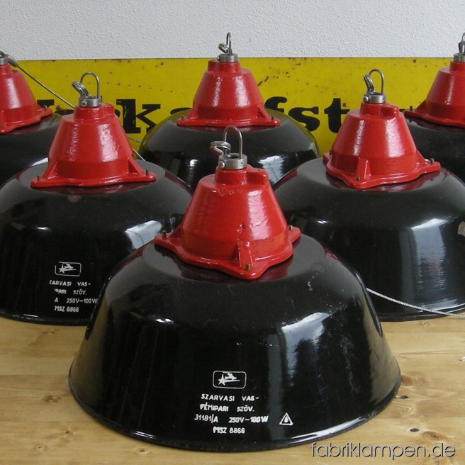 Impressive schwarze Industrielampen mit roten Oberteilen. Material: schwarz  emailliertes Blech und rot lackiertes Gusseisen, mit Drahtseil-Aufhängung.  Höhe Lampen ohne Aufhängeöse ca. 23 cm, Durchmesser Schirm ca. 36 cm. Die Schirme haben eindeutige Alters- und Gebrauchsspuren. 