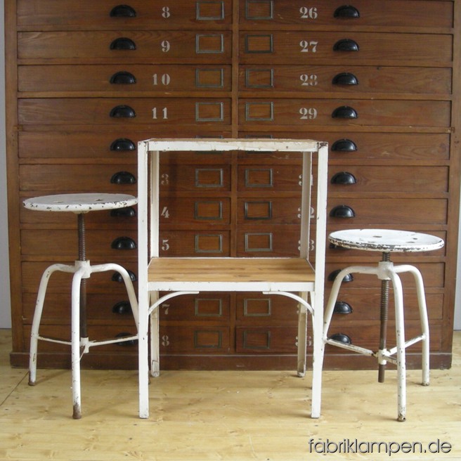 Alter Instrumententisch mit zwei Arzthockern, alles aus Stahl. Alle Teile sind im stark gebrauchten Originalzustand, mit üblichen starken Alters- und Gebrauchsspuren. Die Platten des Tisches sind mit alten Holzplatten ersetzt worden. Abmessungen: Tisch: Höhe ca. 79 cm, Breite ca. 53 cm, Tiefe ca. 43 cm. Hocker: Sitzhöhe ca. 40-64 cm, Durchmesser Sitze ca. 35 cm.