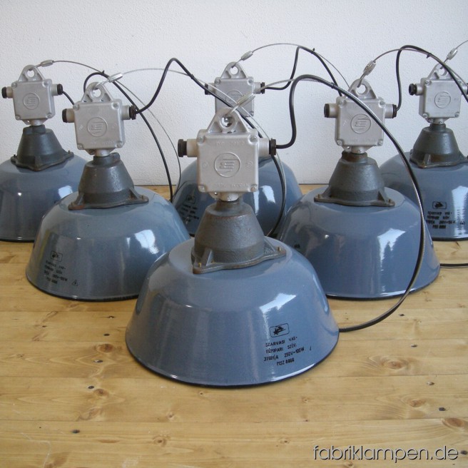 Graue Industrielampen mit gusseisernen Oberteilen und Verteilerdosen aus Aluminium. Die Lampen sind neu elektrifiziert und haben eine Drahtseil-Aufhängung. Material: Gusseisen, Aluminium, Stahl, grau emailliertes Blech. Höhe der Lampen mit Verteilerdosen (ohne Aufhängung) ca. 36 cm, Durchmesser Schirm ca. 36 cm.