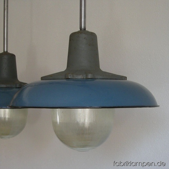 Blaue Emaille Industrielampen mit gusseisernen Oberteilen und Schutzgläser. Die Lampen sind neu elektrifiziert und haben eine Aufhängung aus Stahlrohr mit Baldachin. Material: Gusseisen, Glas, Stahl, blau emailliertes Blech. Höhe der Lampen ohne Aufhängung ca. 34 cm, Durchmesser Schirm ca. 42 cm. Gesamthöhe mit Aufhängung 86 (oder 65) cm.