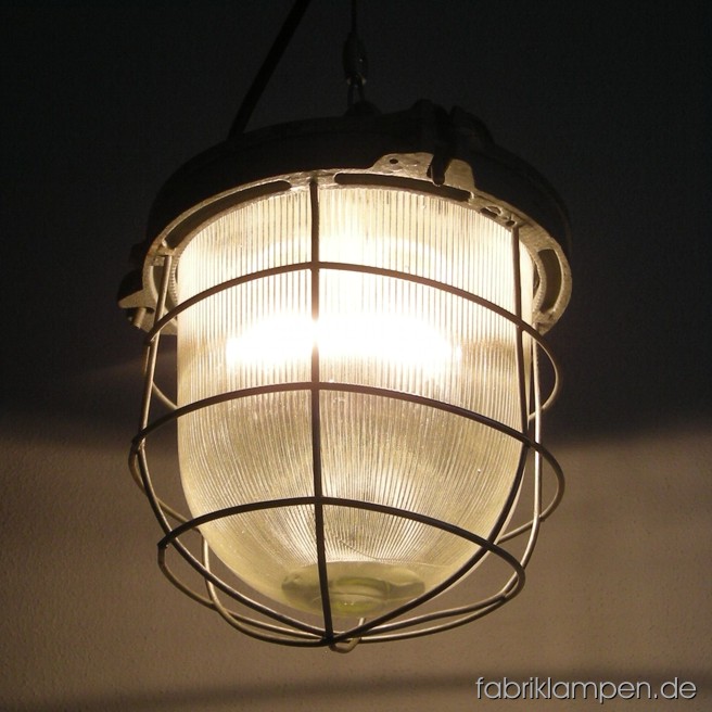 Rundliche Bunkerlampe (Industrielampe) mit gusseisernem Gehäuse, Stahlgitter und Schutzglas. 8 Stück vorhanden. Die Lampen sind gereinigt, montiert mit Drahtseil-Aufhängung, neu elektrifiziert (ausgestattet mit ca. 2 m Kabel) und getestet. Gesamthöhe: ca. 32 cm, Durchmesser ca. 23 cm, Gewicht ca. 6 kg.