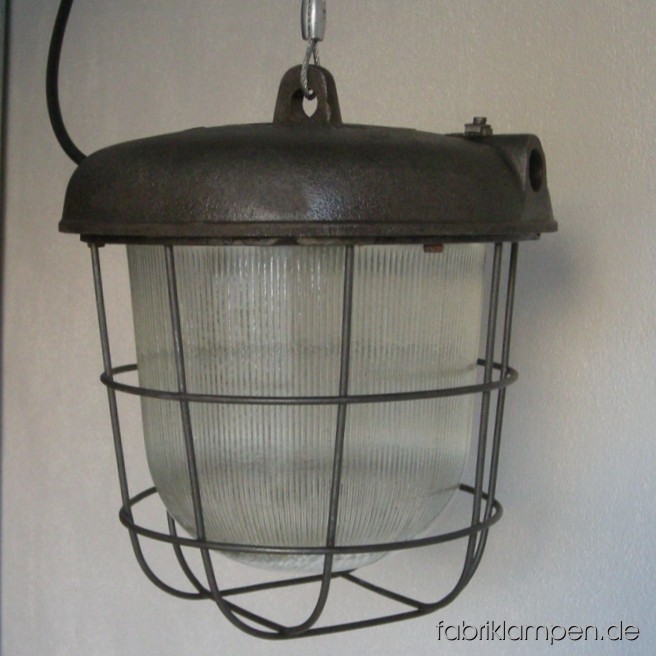 Massive Bunkerlampe (Industrielampe) mit gusseisernem Gehäuse, Stahlgitter und Schutzglas. Wir haben 10 Lampen auf Lager. Die Lampen sind gereinigt, neu elektrifiziert (ausgestattet mit ca. 2 m Kabel) und getestet. Auf Wunsch können die Lampen mit Drahtseil-Aufhängung geliefert werden. Gesamthöhe: ca. 30 cm, Durchmesser ca. 26 cm.