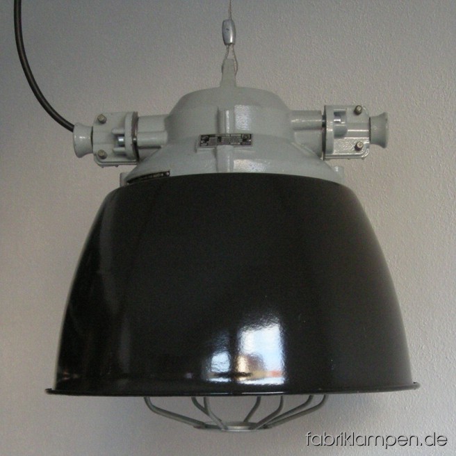 Seltene schwarze Industrielampe im schönen Originalzustand. Diese Lampen bilden einen Übergang zwischen Bunkerlampen und Emaille Lampen – sie sind robuste Bunkerlampen, die mit Emailschirmen versehen wurden. Zur Zeit haben wir 5 Exemplare auf Lager. Die Lampen sind neu elektrifiziert und ausgestattet mit E27 Porzellenfassungen. Material: schwarz (innen weiß) emailliertes Blech, hellgrau lackiertes Aluminium-Oberteil, Stahlgitter, Schutzglas. Höhe der Lampen 39 cm, Durchmesser Schirm ebenso 39 cm.