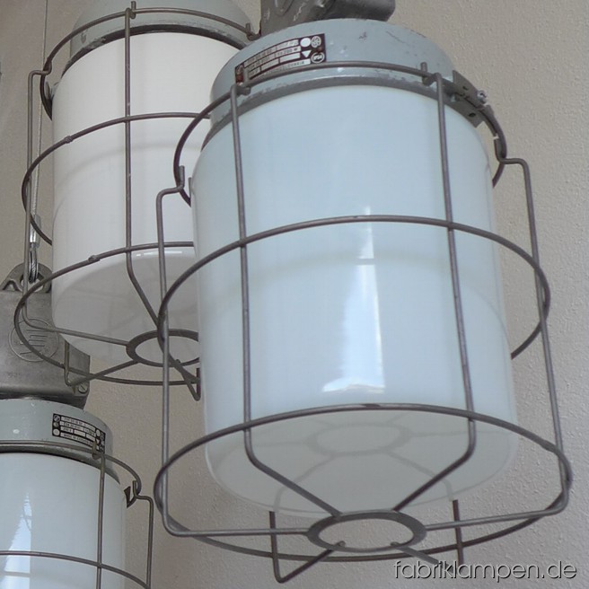 Gracile Gitterlampe mit Glaskolbe. 4 stück auf Lager. Die Lampen sind sehr grazil aufgebaut und daher auch für weniger belastbare Decken geeignet. Die Lampen sind im schönen Originalzustand, aufgearbeitet und neu elektrifiziert. 
Material: Aluminium Gehäuse (grau lackiert) und Verteilerdose (roh), Stahlgitter und Glaskolbe. Die Glaskolben sind entweder aus Milchglas (weiss, unten mit scharfer Kante) oder aus Opalinglas (Kante unten abgerundet). Die Lampen sind mit Drahtseil-Aufhängung und 2 meter Textilkabel ausgerüstet (rot, schwarz, grün immer auf Lager – d. h. sofort leiferbar; andere Farben sind auch möglich), andere Längen sind gegen Aufpreis möglich. Höhe 40 cm, Durchmesser Gitter 20 cm.