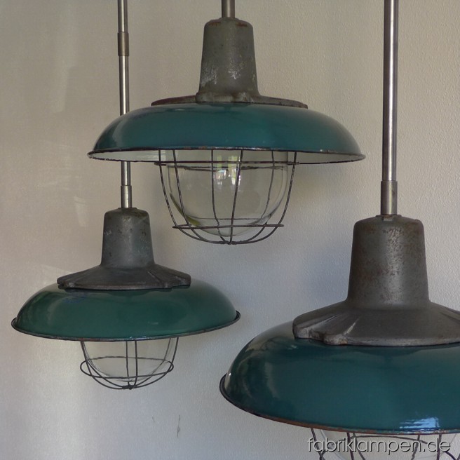 Robuste grüne Fabrikleuchten mit gusseisernen Oberteilen und Schutzgläser. Die schöne grüne Emaille Schirme haben Aufschriften. Diese Lampen haben in zwei Varianten auf Lager: mit Klarem Schutzglas und Strahlgitter (wie abgebildet) oder mit geriffeltem Schutzglas (wie hier). Die Lampen sind neu elektrifiziert und haben eine Aufhängung aus Stahlrohr mit Baldachin. Material: Gusseisen, Glas, Stahl, grün emailliertes Blech. Die Lampen sind mit E27-Porzellanfassungen ausgestattet und mit allen gängigen Leuchtmitteln einsatzbar (incl. LED- und Energiespar-Birnen).