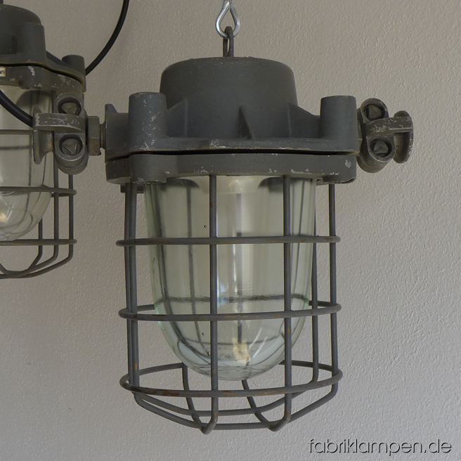 Seltene robuste Bunkerlampe mit Schutzglas und Gitter. Aktuell haben wir 4 Exemplare in dieser Größe und 6 Exemplare der kleineren Version dieser Lampen auf Lager. Die Lampen haben die Spuren der vergangenen Jarhzehnten, sie sind gereinigt und neu elektrifiziert. Material: grau lackiertes Gehäuse aus Aluminium, Schutzgitter, Schutzglas. Höhe der Lampen (ohne Aufhängeöse) 30 cm, Durchmesser (ohne „Ohren“) 20 cm. Sie bekommen die Lampen mit 2 Meter Kabel, ohne Aufhängung.