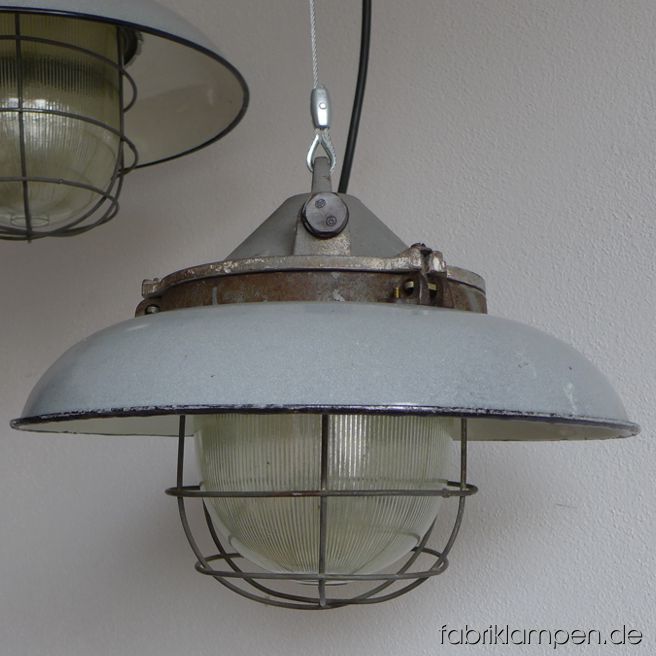 Seltene graue Bunkerlampe mit grauem Emailleschirm. Aktuell haben wir 3 Exemplare auf Lager. Die Lampen haben die Spuren der vergangenen Jarhzehnten, sie sind gereinigt und neu elektrifiziert, ausgestattet mit neuen E27 Porzellanfassungen. Material: grau (innen weiß) emailliertes Blech, gusseisernes Oberteil, Stahlgitter, Schutzglas. Höhe der Lampen 29 cm, Durchmesser Schirm 41 cm.