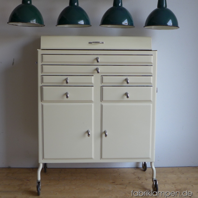 Alter Arztschrank (Arztkommode) um ca. 1950 im sehr schönen Originalzustand. Es handelt sich hier um einen alten Zahnarztschrank oben mit zwei größeren, flacheren und vier kleineren, tieferen Schubläden, unten mit geteiltem Stauraum mit links einem, rechts zwei Regalböden. Der Schrank steht auf Rollen und lässt sich (mit den wunderbaren seitlichen Griffen) leicht zu bewegen. Sehr gut erhalten, schöne Farbe, alles funktioniert und bewegt sich leicht. Für Ihre Dokumente, als Schminkschrank oder für ein Tattoo Salon unentbehrlich… Wir haben aktuell vier ähnliche Schränke auf Lager.