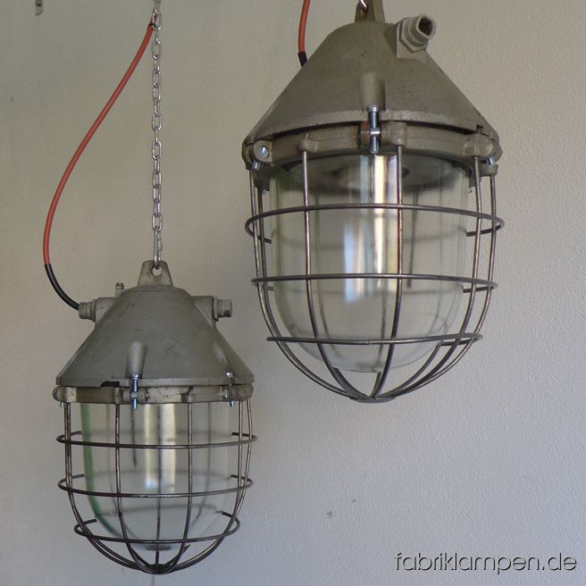 Große Bunkerlampe aus Aluminium mit Schutzglas und Gitter. Aktuell haben wir 35 Exemplare von dem Typ auf Lager, in mehreren Farbvarianten (Gehäuse oben). Die Lampen haben die Spuren der vergangenen Jarhzehnte, sie sind gereinigt, die Roststellen auf dem Gitter behandelt und neu elektrifiziert (ausgestattet mit den originalen E40 Fassungen und Adaptern von E40 auf E27 oder direkt mit neuen E27-Fassungen). Material: Gehäuse aus Aluminium, Schutzgitter, Schutzglas. Höhe der Leuchten ca. 42 cm, Durchmesser ca. 30 cm. Das Gewicht beträgt lediglich 7,3 Kg – die Lampen sind relativ leicht, diese Größe und Gewicht sind zusammen eher selten. Sie bekommen die Lampen mit 2 Meter Kabel (andere Längen sind natürlich möglich), ohne Aufhängung –Kettenaufhängung kann gegen Aufpreis mitgeliefert werden.