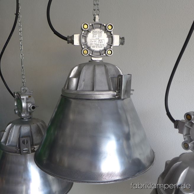 Große Industrielampen aus Aluminium mit Schutzglas, Gitter und Schirm. Aktuell haben wir 20 Exemplare von dem Typ auf Lager. Die Lampen sind aufgearbeitet: Gehäuse und Schirme entlackt und geschliffen (nicht hochlanzpoliert, mit Spuren der Poliermaschine). Die Schirme sind innen weiss lackiert, somit Sie ein freundliches Licht haben. Die Leuchten sind neu elektrifiziert und ausgestattet neuen E27-Fassungen. Unsere Empfehlung für die Leuchten sind die LED Birnen (zum Beispiel in warmweiss). Material: Gehäuse und Schirm aus Aluminium, Schutzgitter aus Stahl, Schutzglas. Höhe der Leuchten ca. 52 cm, Durchmesser ca. 46 cm. Das Gewicht beträgt rund 10 Kg. Sie bekommen die Lampen mit 2 Meter Kabel (andere Längen sind natürlich möglich), ohne Aufhängung – Kettenaufhängung kann gegen Aufpreis mitgeliefert werden. Die Lampen sind auch als Bunkerlampe einsetzbar, ohne Schirm (Höhe 46 cm, Durchmesser 26 cm). Wir haben einige Exemplare mit anderen Verteilerdosen oben (letztes Bild).