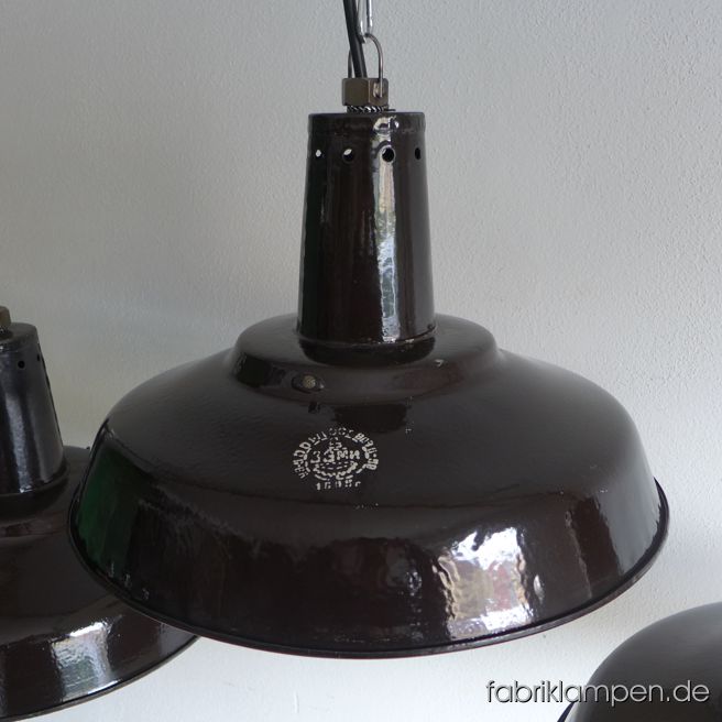 Alte schwarze Emaille Industrieleuchten mit Herstellermarke. Die Lampen haben die deutlichen Spuren der vergangenen Jahrzehnte (Abplatzer, Roststellen, Kratzer, Verfärbungen and Co.). Sie sind gereinigt und neu elektrifiziert (E27 Porzellanfassung). Material: schwarz (innen weiß) emailliertes Stahlblech – die schwarze Farbe ist manchmal etwas bräunlich. Im oberen Halsbereich mit Löchern (für Lüftung/Kühlung), innen mit Halterung für Gläser. Die Lampen werden ohne Gläser geliefert – sie waren früher auch ohne Gläser im Gebrauch. Die Lampen sind ziemlich groß, trotzdem nicht klobig, da der Schirm nicht sehr hoch ist. Die Lampen werden mit Aufhängeöse und 2 Meter Kabel geliefert (andere Längen sind natürlich möglich), auf Wunsch können sie auch mit Textilkabel und Ketten- oder Stahlrohr-Aufhängung ausgestattet werden (gegen Aufpreis). Durchmesser 46 cm, Höhe 30 cm. Wir haben auch die kleinere Variante auf Lager: Durchmesser 39 cm, Höhe 24 cm.
