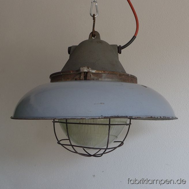 Sehr massive und schwere große Bunkerlampe mit Emailleschirm in grau (hellgrau). Diese Lampe ist DER Hammer: der Schirm hat einen Durchmesser von 52 cm, mit massiven gusseisernem Oberteil und Glaskolben wiegt die Lampe stolze 15 kg. Sie ist die größte ihrer Art und extrem selten zu finden. Diese Lampe besteht aus einem schweren gusseisernen Oberteil mit Schutzglas (geriffeltes Thermoglas) und Schutzgitter und einem grau (innen weiß) emaillierten Schutzschirm aus Stahlblech. Die Lampen haben die üblichen Spuren der vergangenen Jahrzehnte (Abplatzer, Kratzer, Verfärbungen, kleinere Roststellen, und Co.). Wir haben diese alle behandelt. Die Leuchten sind gereinigt und neu elektrifiziert (mit E27 Fassung). Die Abmessungen: Durchmesser 52 cm, Höhe 39 cm, Gewicht 15 Kg. 
Die Lampen werden mit 2 Meter Kabel geliefert (andere Längen sind natürlich möglich). Um diese massiven Industrielampen verwenden zu können, brauchen Sie eine tragfähige Decke – oder starke Balken, die diese recht gewichtigen Leuchten  halten können. 