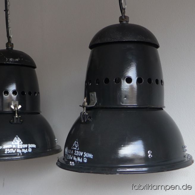 Alte antike schwarze Fabriklampen mit Aluminium (teilweise gusseisernem) Deckel und gelochtem Hals. Sehr charakteristischer Aufbau, mit vielen Schrauben – Industriedesign pur. Die Lampen haben die Spuren der vergangenen Jahrzehnte (Verfärbungen, kleine Abplatzer, Roststellen and Co. – wir haben die alle behandelt). Sie sind gereinigt und neu elektrifiziert (E27 Keramikfassung). Material: schwarz (anthrazit) emailliertes Stahlblech, Aluminium (manchmal Gusseisen). Die Form ist kompakt, sie wirkt nicht robust, kann universal eingesetzt werden – diese Fabriklampen sind sowohl für größere Räume (Gastronomie) als auch für Wohnbereiche (über Tisch, Theke etc.) geeignet. Der ultimative Eye-Catcher. Sie bekommen die Lampen mit 2 Meter Kabel (andere Längen sind natürlich möglich) und massiven Aufhängeösen für die sichere Aufhängung. Gegen Aufpreis können die Lampen auch mit Ketten-Aufhängung geliefert werden. Die Abmessungen: Durchmesser Lampe (Schirm) 44,5 cm, Höhe 44 cm.  