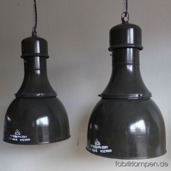 Sehr große antike Emaille Industrielampen mit Aufschrift – in dieser Form und Größe eher selten. Die Lampen haben die starken Spuren der vergangenen Jahrzehnte (Verfärbungen, Abplatzer, Roststellen: alle von uns behandelt), sie sind gereinigt und neu elektrifiziert (E40/E27 Keramikfassung/en). Material: schwarz (anthrazit) emailliertes Stahlblech. Wir haben auch einige graublaue Exemplare (mit deutlichen Alters- und Gebrauchsspuren) auf Lager. Sie bekommen die Lampen mit 2 Meter Kabel (andere Längen oder Textilkabel sind natürlich möglich) und massiven Aufhängeösen für die sichere Aufhängung. Gegen Aufpreis können die Lampen auch mit Ketten-Aufhängung geliefert werden. Klassische Form, große Ausführung - nur für Räume mit entsprechender Raumhöhe empfohlen. Die Abmessungen: Durchmesser Lampe (Schirm) 41 cm, Höhe 64 cm. 