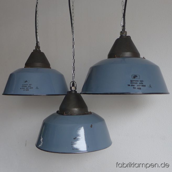 Alte graublaue Emaille Industrielampen mit gusseisernem Oberteil, mit Herstellermarke. Die Farbe ist graublau, nach RAL-Skala ca. Taubenblau (RAL 5014). Wir haben diese Lampen auch in Richtung grau bzw. blau auf Lager. Die Lampen haben die Spuren der vergangenen Jahrzehnte (Abplatzer, Roststellen, Kratzer, Verfärbungen und Co. – wir haben die alle behandelt), sie sind gereinigt und neu elektrifiziert, ausgestattet mit neuen E27 Keramikfassungen. Material: graublau emailliertes Stahlblech, gusseisernes Oberteil. Sie bekommen die Lampen mit 2 Meter Kabel (andere Längen oder Textilkabel sind natürlich möglich) und massiven Aufhängeösen für die sichere Aufhängung. Gegen Aufpreis können die Lampen auch mit Ketten-Aufhängung oder Stahlrohr-Aufhängung und Baldachin geliefert werden. Die Abmessungen: Durchmesser Lampe (Schirm) 41 cm, Höhe 28 cm. 