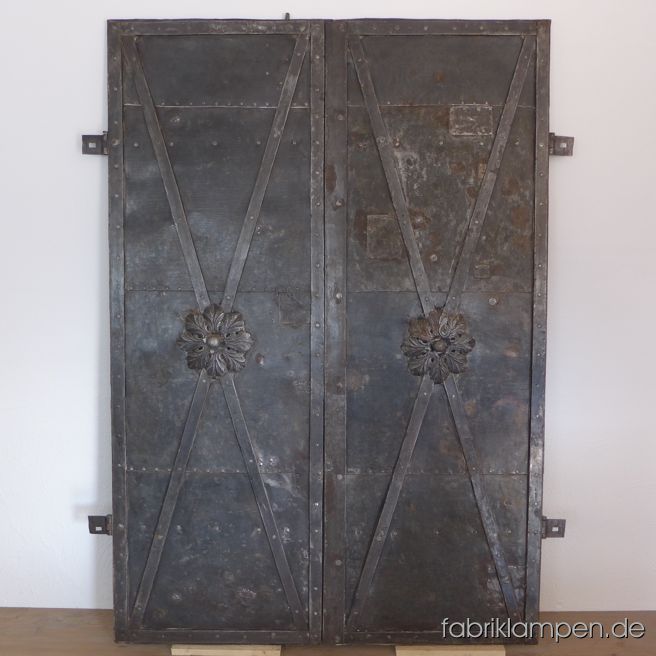Alte, antike Eisentür, geschmiedet (ähnlich wie eine Fetzentür, etwas jünger). Die zweiflügelige Türe stammt aus einem Gebäude, die um 1820 gebaut wurde. Wunderschöne Schmiedearbeit mit großen Zierrosetten und zahlreichen kleinen Unebenheiten. Das Blech wurde im Laufe der Zeit hier und da geflickt. An Blechstücken sind noch die kleinen unregelmäßigen Rillen zu sehen, die während der Herstellung entstanden. In der Rosette mit wunderschönen kleinen Details. Die komplette Türe ist mit Handarbeit hergestellt worden. Mit funktionierendem (gefedertem) Schließmechanismus (von innen kann man die Türe schließen). Die Türe ist intakt, keine Durchrostung oder Ähnliches ist festzustellen. Sie ist gerade, nicht verzogen, die zwei Flügel passen perfekt zusammen. In diesem Zustand sehr schwer zu finden. Sie ist gereinigt und konserviert (Hartöl/Hartwachs). Sofort einsetzbar. Höhe: 184 cm, Breite 134 cm (ohne Scharniere).  