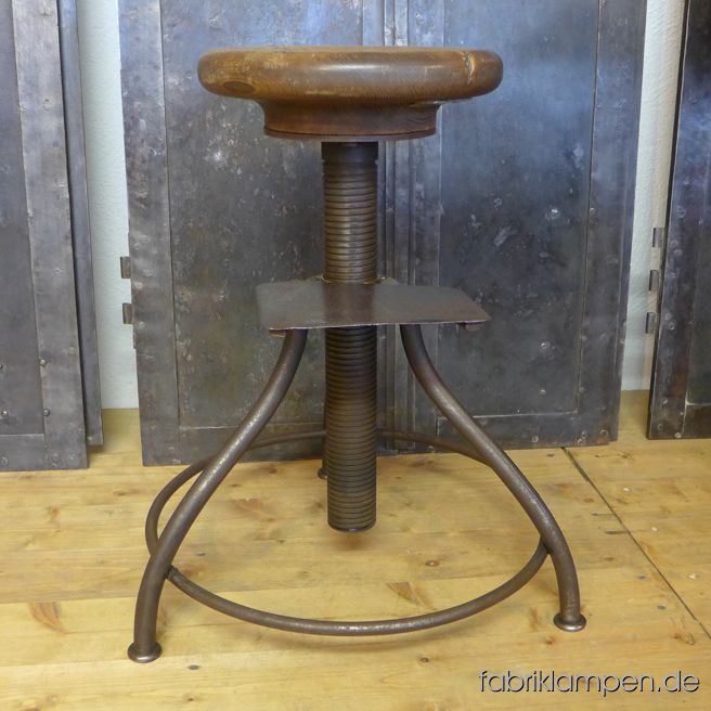 Antiker alter höhenverstellbarer Industriehocker (Drehhocker) mit Eichensitz. Sehr schöne, interessante Form mit geschwungenen Linien. Brutal starke Ausführung, die Spindel ist 5 cm stark, sie bewegt sich in einer Messingmutter (nach ca. 100 Jahren Gebrauch ist es in höheren Positionen etwas locker, der Hocker kann noch gebraucht werden). Alter: ca. um 1920. Der Sitz (gemacht aus einem Stück Eichenholz) hat eine wunderbare Patina und ist mit Naturwachs behandelt. Die Sitzplatte ist 4,5 cm stark und hat eine angenehme Sitzmulde. Der Durchmesser des Sitzes beträgt 29 cm. Massive, unverwüstliche Ausführung. Die Sitzhöhe erlaubt die Nutzung auch bei höheren Tischen/Theken. Bestens geeignet als Gitarrenhocker. Zum Hocker gehört eine abnehmbare Fußstütze. Diese ist im Laufe der Jahrzehnte abgetreten worden, sodass der Rand scharf wie eine Axt ist. Daher ist bei dem Gebrauch der Fußstütze Vorsicht geboten! Sitzhöhe von 49 bis 72 cm (ganz hoch geschraubt etwas wackelig).
 