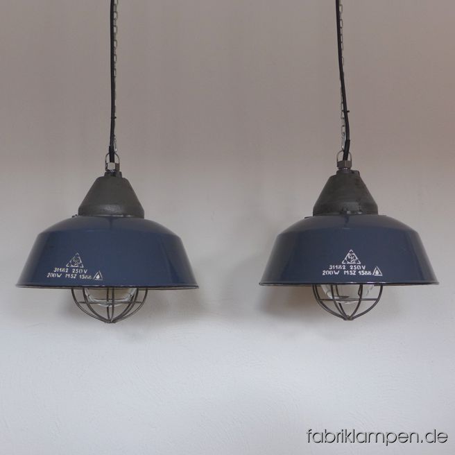 Emaille Industrielampe, alte dunkelblaue Fabriklampe mit gusseisernem Oberteil, Emailleschirm im seltenen blauen Farbton (Herstellermarke), Glas & Gitter. Die Lampen haben moderate Spuren der vergangenen Jahrzehnte (Abplatzer, Roststellen, Kratzer, Verfärbungen und Co.). Sie sind gereinigt und neu elektrifiziert, mit neuen E27 Keramikfassungen. Material: dunkelblau emailliertes Stahlblech, gusseisernes Oberteil, Schutzglas und Stahlgitter. Sie bekommen die Lampen mit 2 Meter Kabel und massiven Aufhängeösen für die sichere Aufhängung. Gegen Aufpreis können die Lampen auch mit Ketten-Aufhängung geliefert werden. Die Abmessungen: Durchmesser Lampe (Schirm) 41 cm, Höhe 36 cm. 
