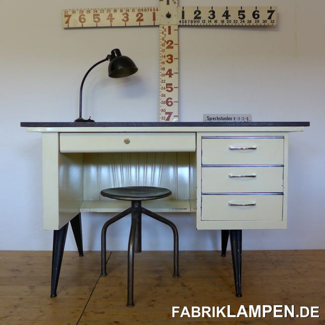 Alter Arztschreibtisch aus den 1950er Jahren. 

Sehr stilvoller Arztschreibtisch aus einer ehemaligen Praxis. Schöne, interessante Form, mit typischen Linien der 1950er Jahre, Rockabilly. 

Der Tisch hat noch die originale Lackierung in Elfenbein, hier und da mit Abplatzungen und kleinen Beschädigungen. Wir haben ihn gründlich gereinigt und die Stellen ohne Lack konserviert. Die große Schublade hat einen neuen Schloss (Burgwächter) bekommen, der Tisch wird mit zwei Schlüsseln geliefert. 
Der Arzttisch hat eine praktische zentrale Verriegelung: ist die große Schublade zu, können auch die seitlichen Schubladen nicht geöffnet werden. 

Die alte Tischplatte war nicht zu retten. Der Tisch hat eine Platte bekommen – aus Eiche massiv, schwarz gebeizt. 

Die klaren Linien, schönen Füße und die sehr seltene fächerförmige Verzierung der Hinterwand prädestinieren diesen Tisch, mitten im Raum platziert zu werden. 

Ein schönes Original, in der Form ziemlich selten. 

Die Abmessungen: Höhe 77 cm, Breite 125 cm, Tiefe 65 cm. 